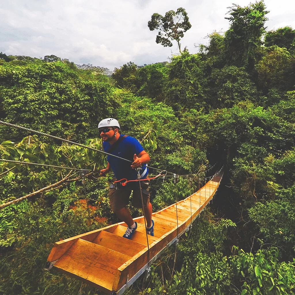 Ecoprojects. Parque Tenamit Maya. Persona subiendo escaleras de madera sobre selva.