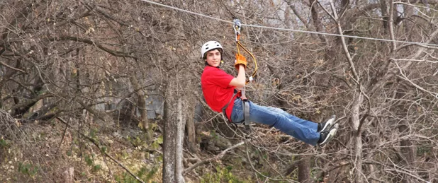 Ecoproparks. Persona usando tirolesa sobre bosque seco.