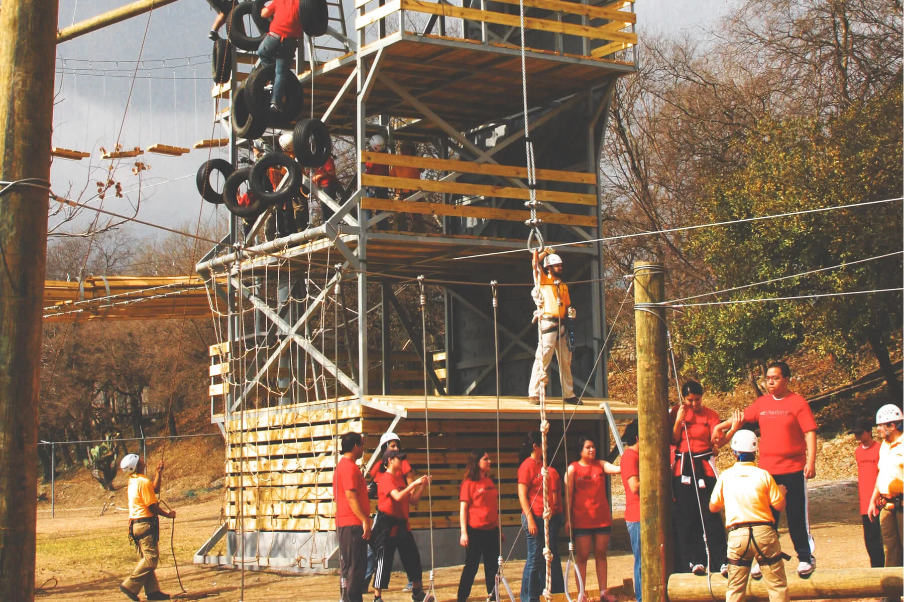 Ecoproparks. Personas ensayando para usar una tirolesa al lado de una torre de aventura.